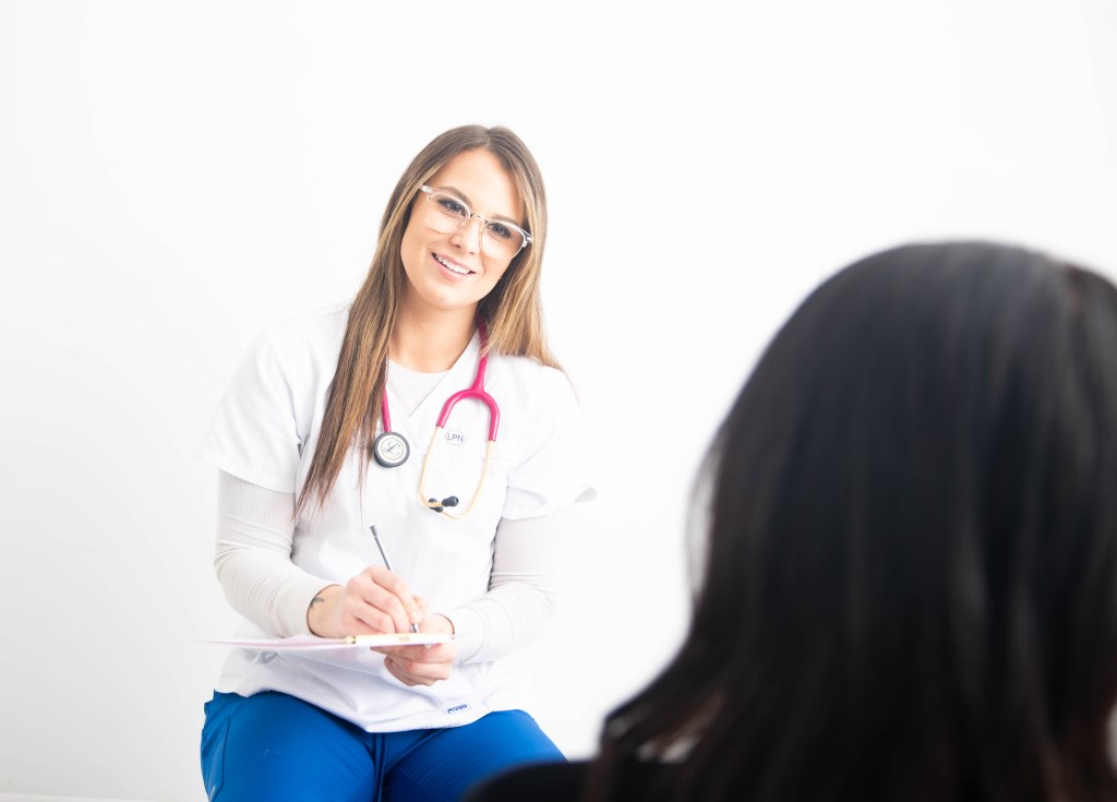 Jessie, owner and foot care clinician at Jessie’s Foot Care, smiling and taking notes during a patient consultation in a bright white clinic.