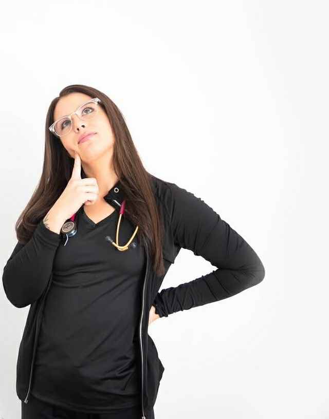 Jessica Power, foot care specialist, stands thoughtfully with her hand on her cheek looking up above her with her stethoscope around her neck.