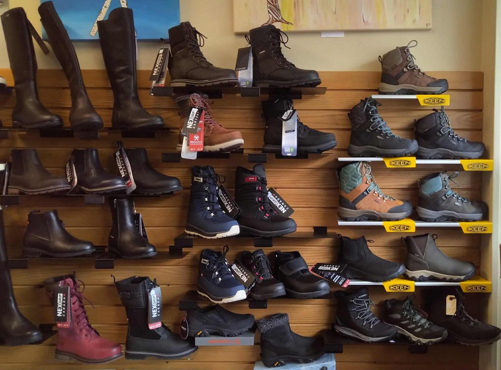 Display of various winter boots on wall shelves at River Valley Footwear, including tall black boots, ankle boots, and insulated hiking-style boots in different colours and styles.